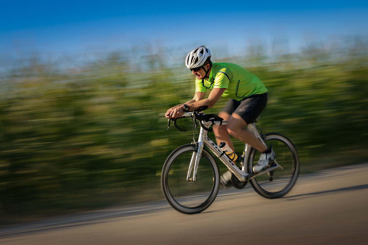 Cyclist riding a road bike past green fields